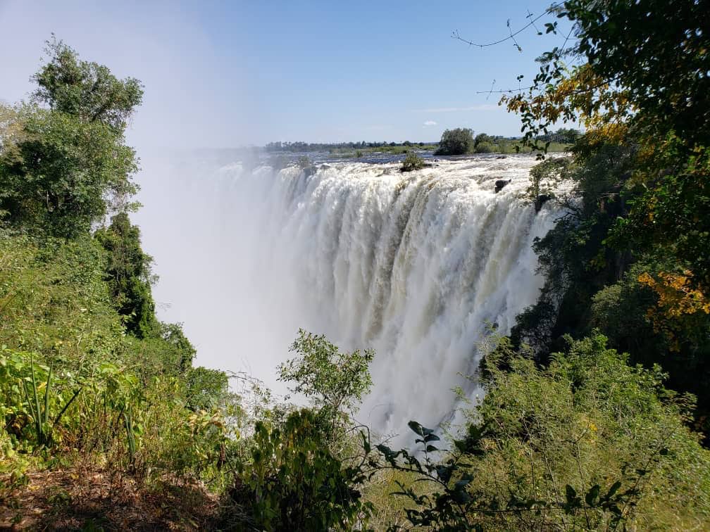 a large waterfall with trees and blue sky Zambia