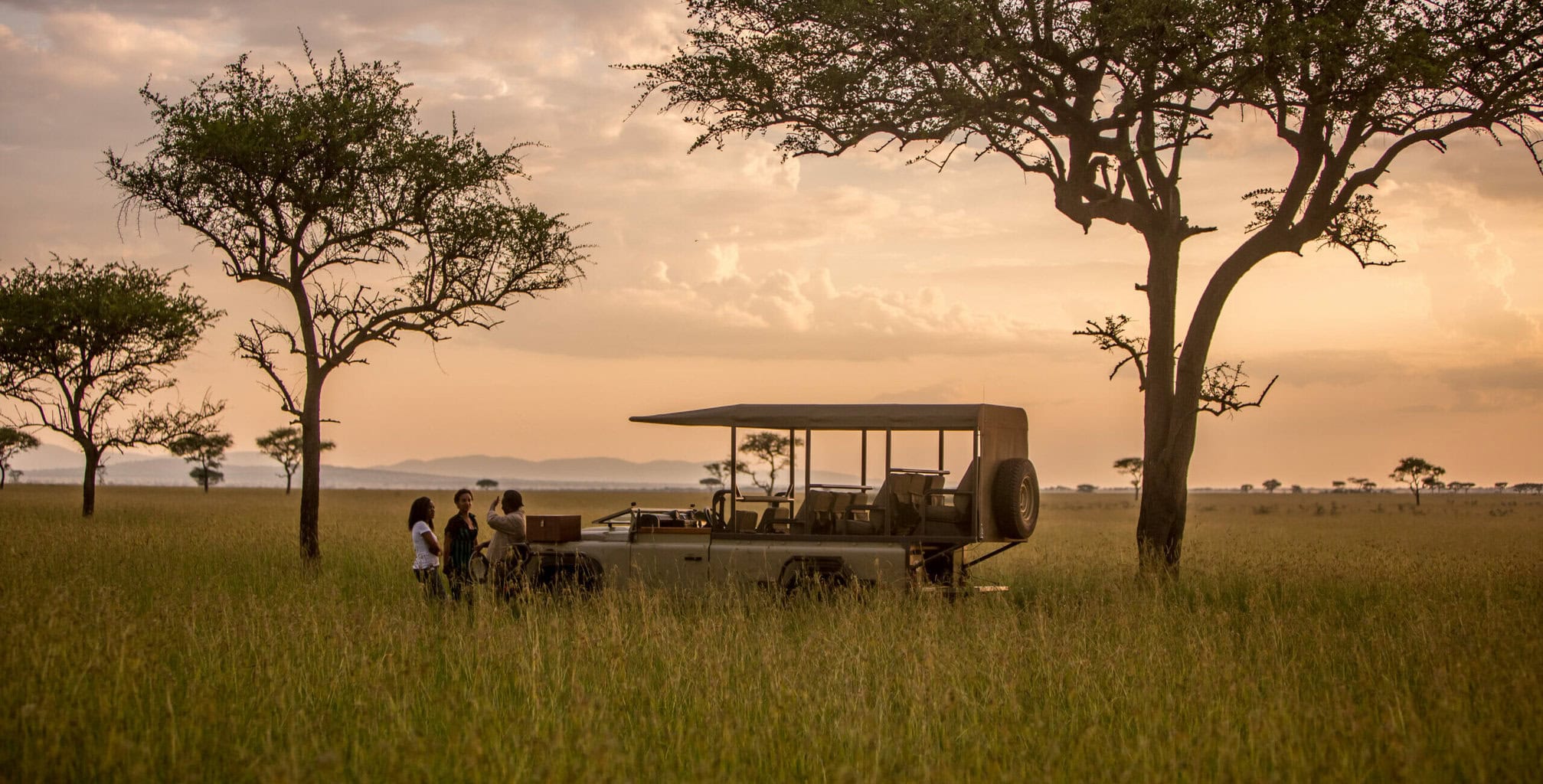 a group of people standing in a field with a vehicle. Tanzania